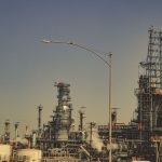 Grande instalação industrial com tubulações e torres metálicas sob céu azul.