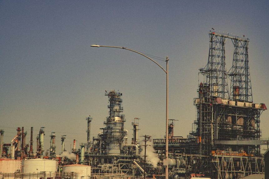 Grande instalação industrial com tubulações e torres metálicas sob céu azul.