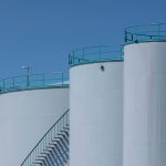 Grandes tanques industriais de armazenamento com estruturas verdes contra um céu azul.