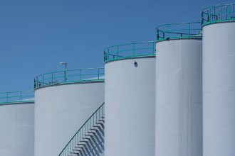 Grandes tanques industriais de armazenamento com estruturas verdes contra um céu azul.
