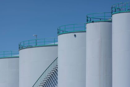 Grandes tanques industriais de armazenamento com estruturas verdes contra um céu azul.