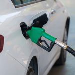 Bico verde abastecendo um carro branco em um posto de combustíveis.