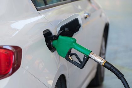 Bico verde abastecendo um carro branco em um posto de combustíveis.