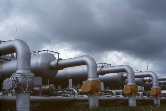 Tubulações e válvulas metálicas de uma instalação industrial de gás sob céu nublado.