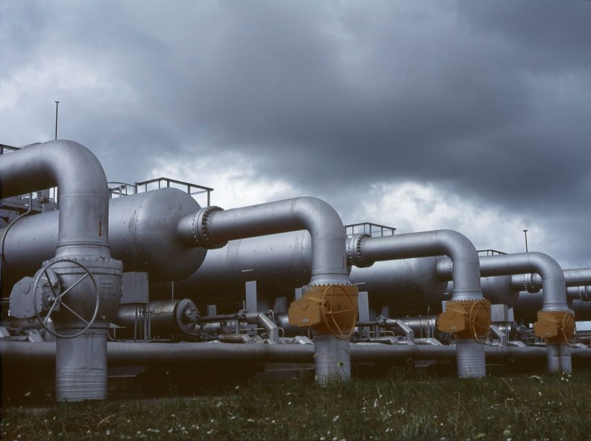 Tubulações e válvulas metálicas de uma instalação industrial de gás sob céu nublado.