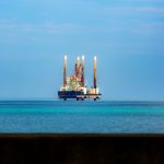 Plataforma de petróleo vista ao longe em meio ao oceano, sob céu claro.