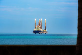 Plataforma de petróleo vista ao longe em meio ao oceano, sob céu claro.