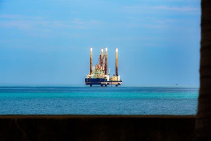 Plataforma de petróleo vista ao longe em meio ao oceano, sob céu claro.